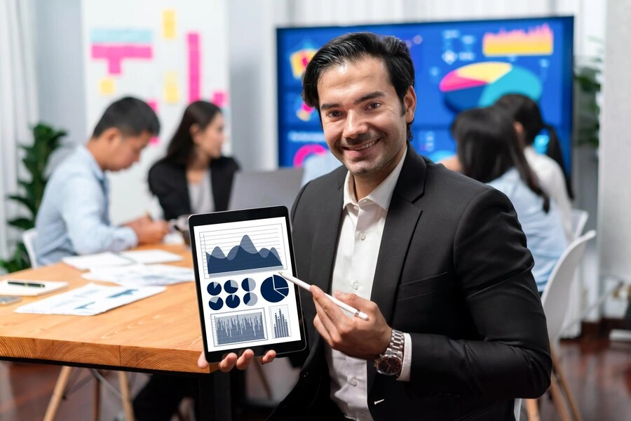 Digital Marketing Agency in Canada: Your Trusted Digital Marketing Partner 18 Businessman-showing-graphs-and-data-on-tablet-in-meeting-room-with-team