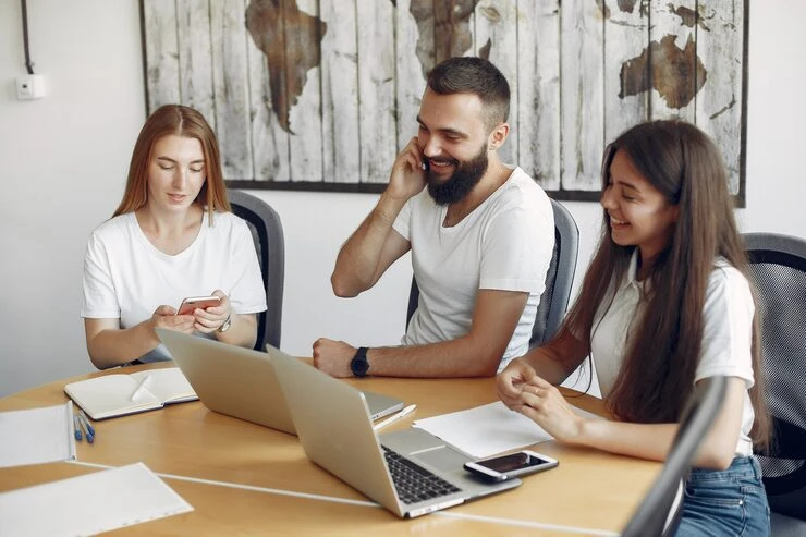 Three professionals collaborating with laptop and mobile devices in relaxed modern office environment