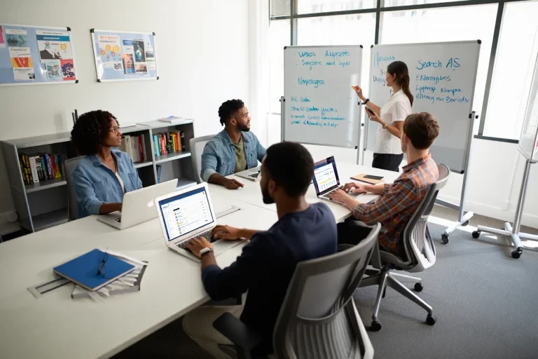 Marketing team developing Google search ad copy on laptops while strategist presents campaign ideas on whiteboard